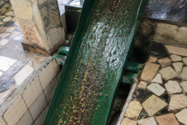 Phone photo of the green discharge chute sloping down from the pulper into a tiled channel